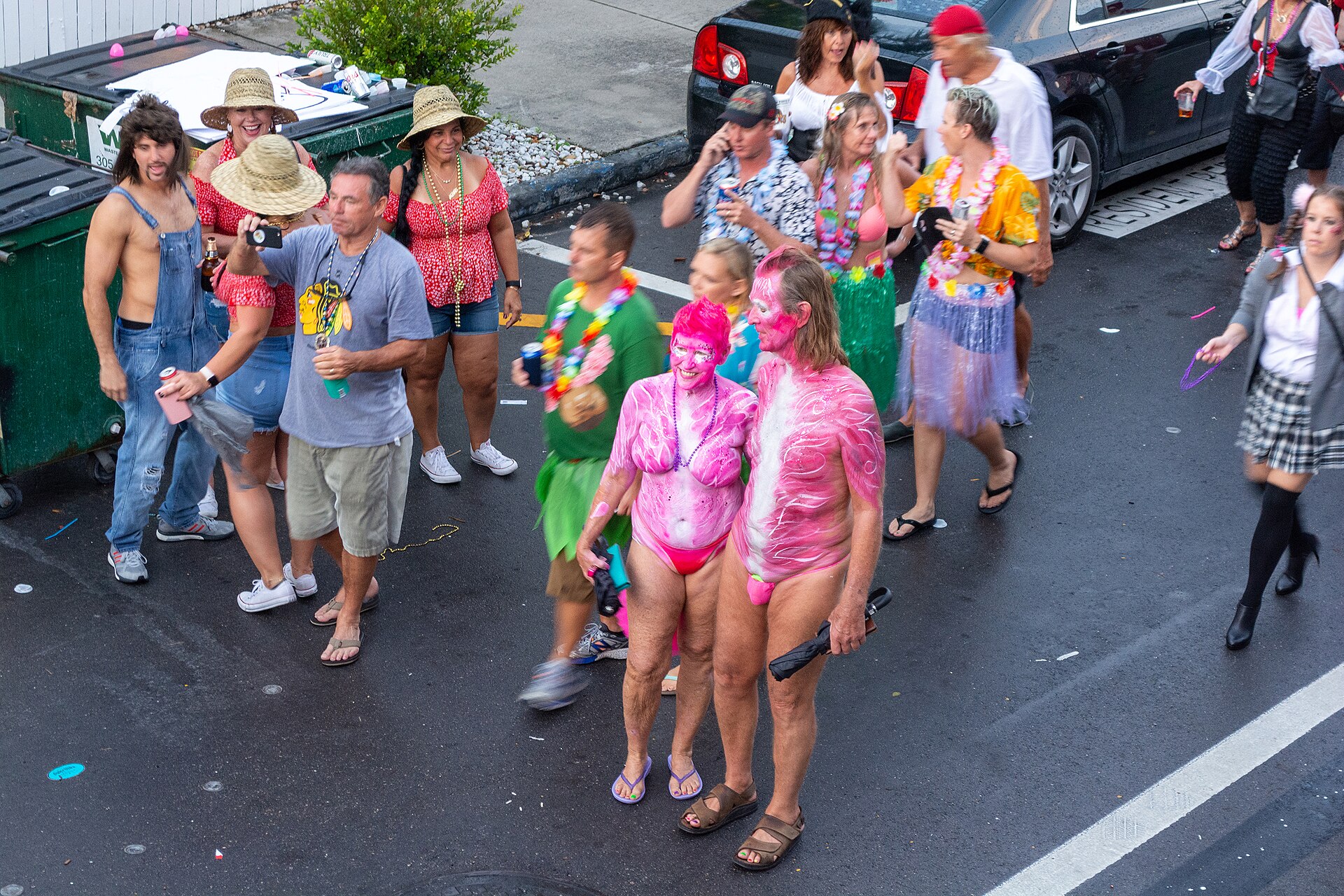 Two participants in pink body paint and costume coverings pause among other Masquerade March revelers in Key West in 2019.